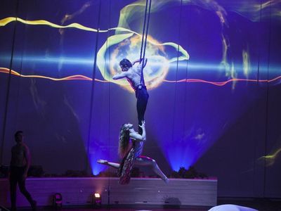 Two aerial performers gracefully execute acrobatics on stage, showcasing their skills against a vibrant backdrop of lights.
