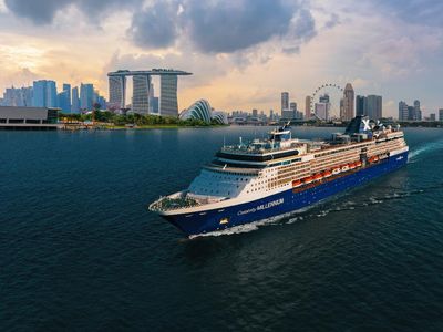 A cruise ship named Celebrity Millennium sails in the water with a vibrant city skyline visible in the background.